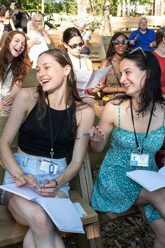 Boston Ballet Summer Dance Program attendees sit together at the outdoor stage, giggling with one another.