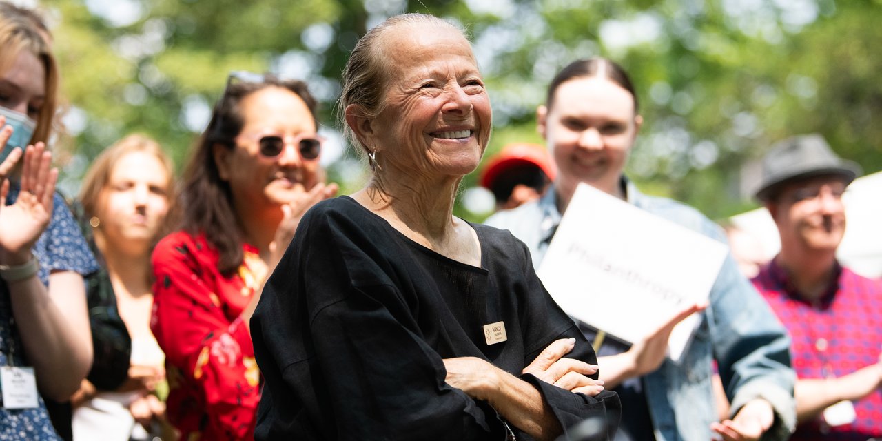 A Board of Trustee brightly smiling, surrounded by staff clapping.