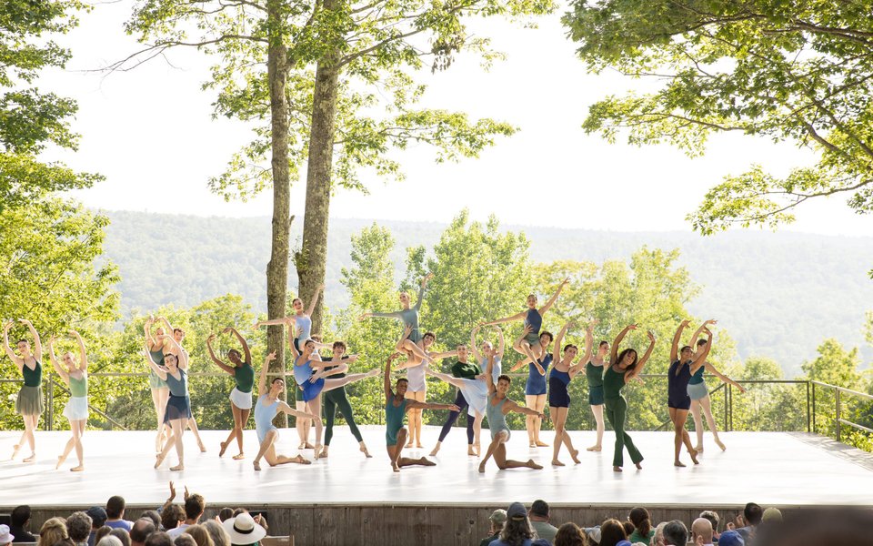 A group of ballet dancers pose in classical positions on the outdoor stage.