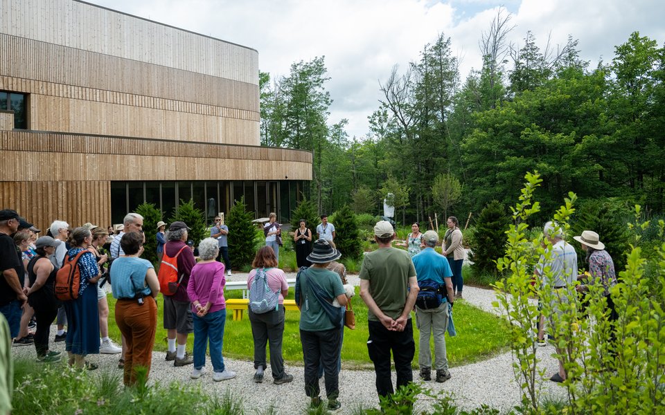 A large group of people stand gathered in a circle at the Indigenous Garden outside of the Doris Duke Theatre.