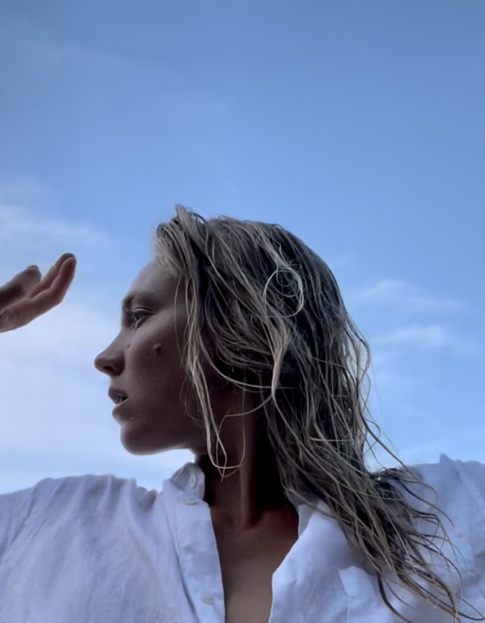 Image of a female-presenting dancer with blonde hair wearing a white shirt and raising their arms toward the sky.