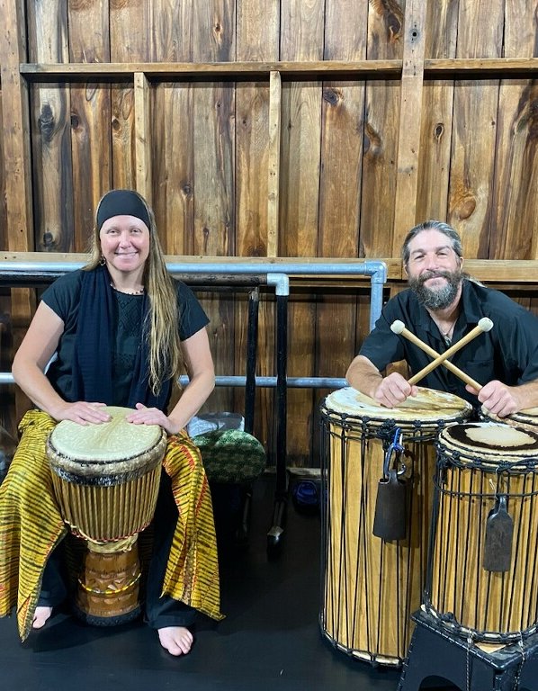 Two people with African drums smile for the camera.