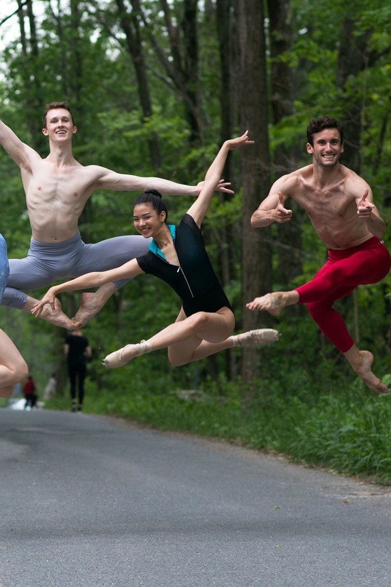 Contemporary Ballet Dancers of The School jumping in the air on a road lined with forest foliage.