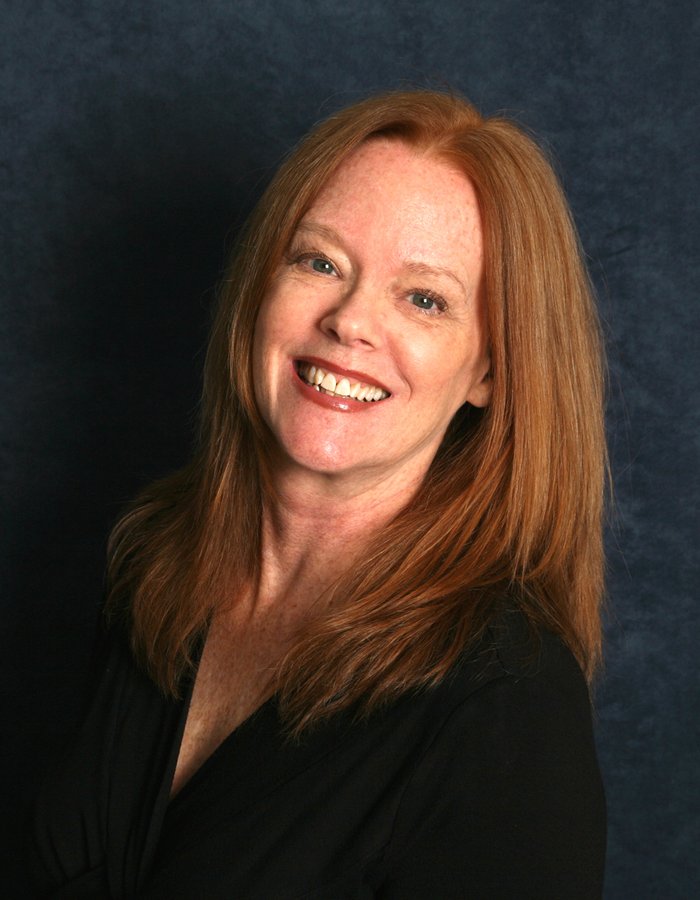 A woman with red hair and blue eyes poses for the camera. Sandy Russell, instructor for Family Music and Dance.