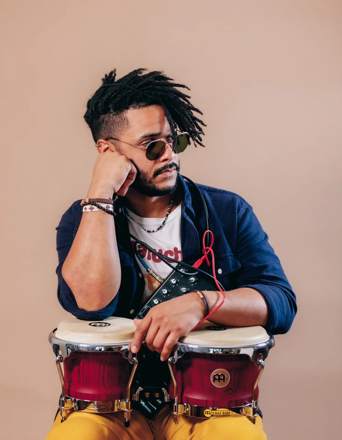 A man poses for a headshot, leaning his elbow over two drums he holds in front of him.