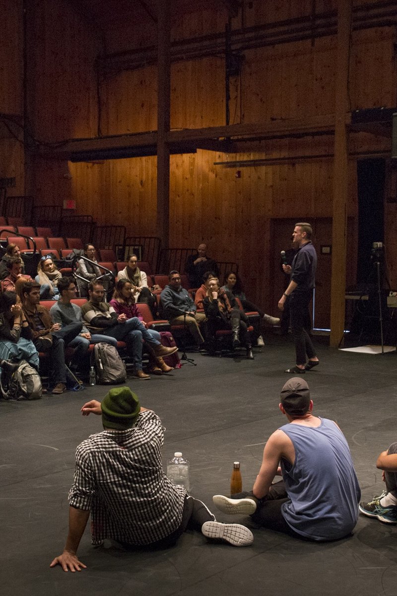 After a Creative Development Residency showing, audience members sit in theater seats listening as the artists sit on the stage floor.